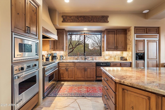 kitchen featuring light stone countertops, custom exhaust hood, a sink, decorative backsplash, and built in appliances