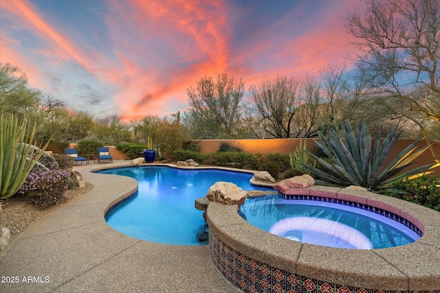 pool at dusk with a patio area and a pool with connected hot tub