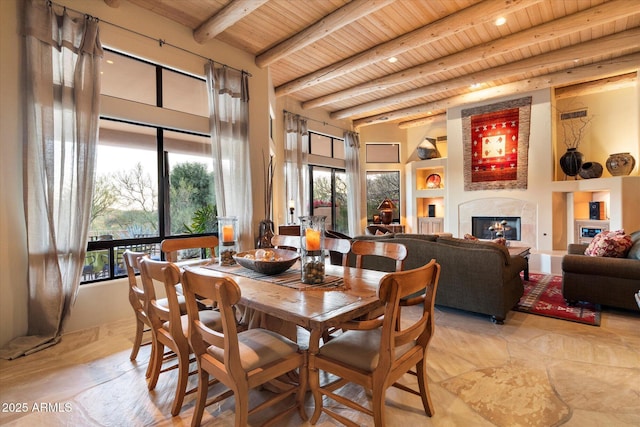 dining area with a glass covered fireplace, beam ceiling, a high ceiling, and wooden ceiling