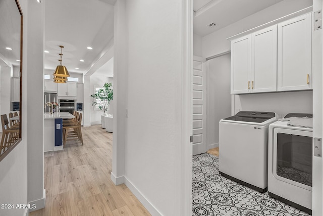 washroom with washing machine and clothes dryer, cabinets, and light hardwood / wood-style floors