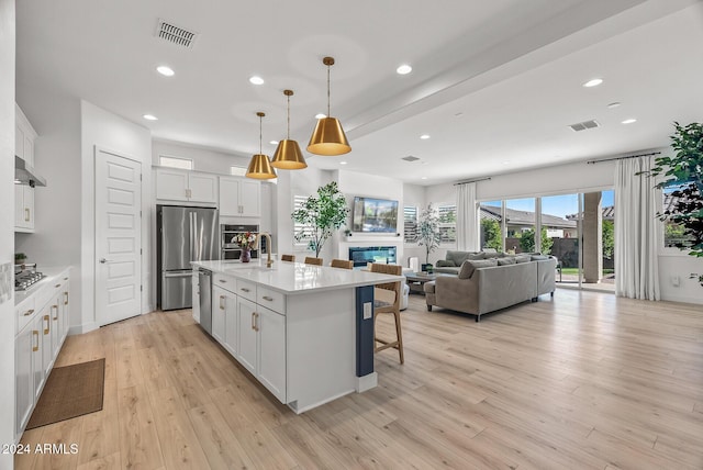 kitchen featuring white cabinetry, hanging light fixtures, light hardwood / wood-style flooring, an island with sink, and appliances with stainless steel finishes