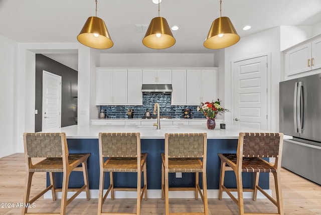 kitchen featuring a center island with sink, decorative light fixtures, light hardwood / wood-style floors, and stainless steel refrigerator