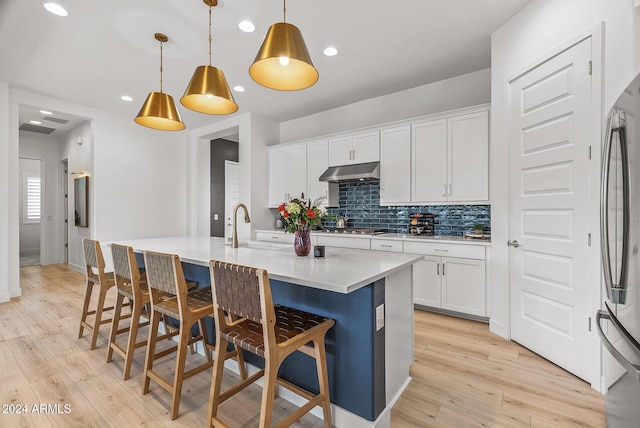 kitchen featuring light wood-type flooring, decorative light fixtures, white cabinetry, and a center island with sink