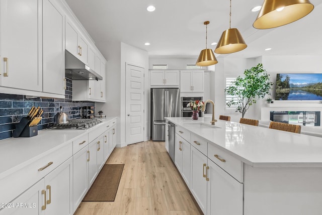 kitchen with pendant lighting, a kitchen island with sink, white cabinets, light wood-type flooring, and appliances with stainless steel finishes