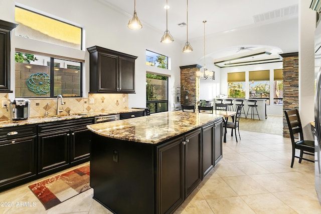 kitchen featuring light stone countertops, a center island, sink, hanging light fixtures, and backsplash