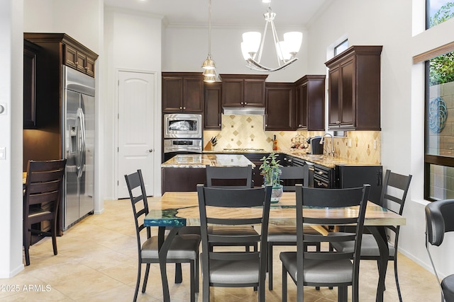 kitchen with light stone countertops, built in appliances, an inviting chandelier, a kitchen island, and hanging light fixtures