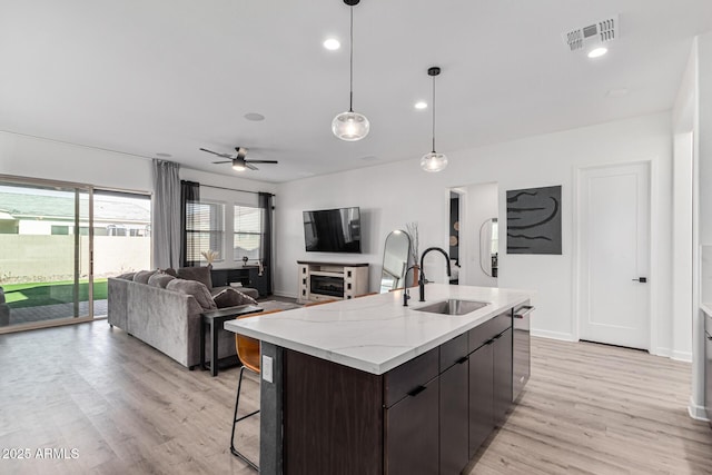 kitchen featuring dark brown cabinets, a kitchen island with sink, ceiling fan, sink, and decorative light fixtures