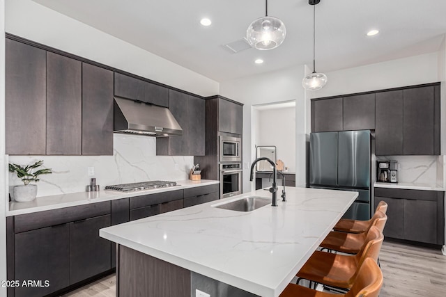 kitchen with a center island with sink, appliances with stainless steel finishes, pendant lighting, and ventilation hood