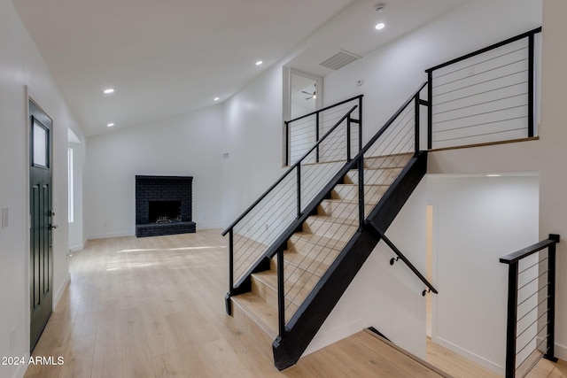 stairway with a fireplace, ceiling fan, hardwood / wood-style floors, and vaulted ceiling