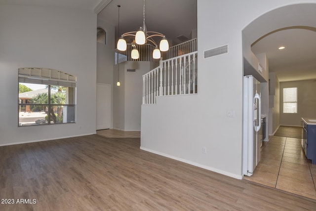 unfurnished dining area featuring hardwood / wood-style flooring, a towering ceiling, a chandelier, and a wealth of natural light