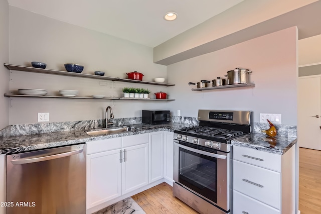 kitchen with open shelves, dark stone countertops, a sink, white cabinetry, and stainless steel appliances