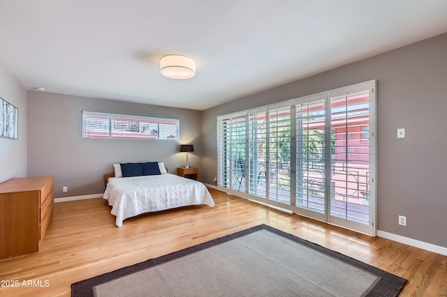 bedroom with access to exterior, light wood-style floors, and baseboards