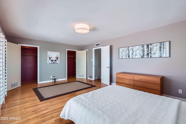 bedroom featuring two closets, baseboards, visible vents, and light wood finished floors