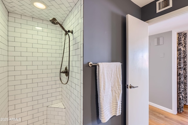 full bathroom featuring a tile shower, visible vents, baseboards, and wood finished floors