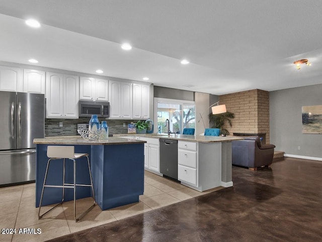 kitchen with a kitchen bar, appliances with stainless steel finishes, decorative backsplash, a kitchen island, and white cabinetry