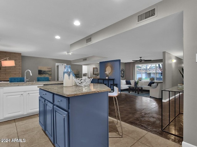 kitchen featuring a breakfast bar, dark stone counters, ceiling fan, a kitchen island, and white cabinetry