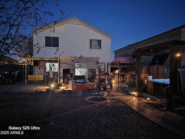 back of house at night with a gazebo, a patio, and stucco siding