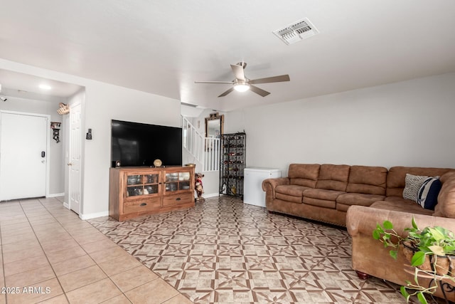 living room with light tile patterned floors, baseboards, visible vents, a ceiling fan, and stairway