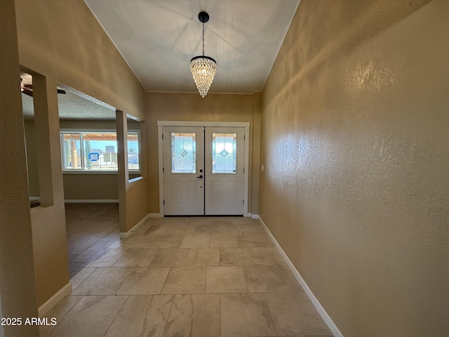 doorway to outside with a notable chandelier, baseboards, and a textured wall