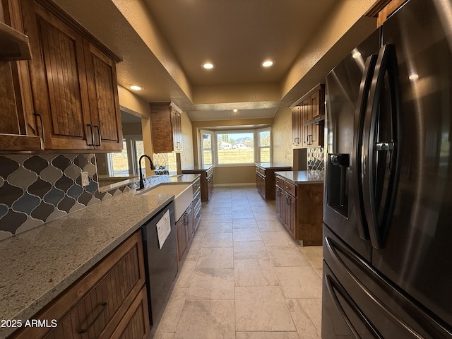 kitchen with black appliances, a sink, stone countertops, backsplash, and a raised ceiling