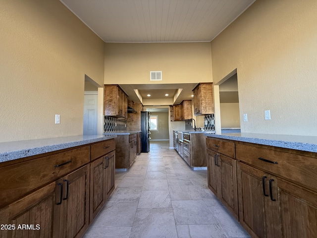 kitchen featuring light stone countertops, visible vents, freestanding refrigerator, a sink, and a textured wall