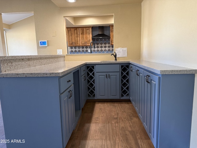 kitchen with a peninsula, dark wood-type flooring, wall chimney range hood, and a sink