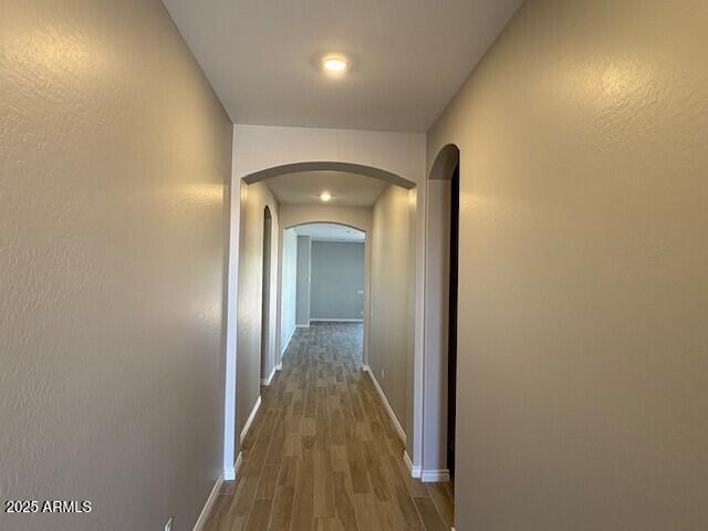 hallway with a textured wall, baseboards, dark wood finished floors, and arched walkways
