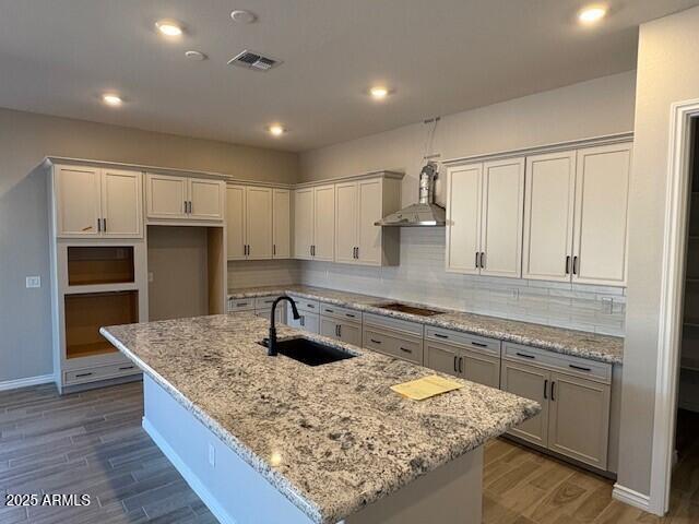 kitchen featuring a sink, black electric stovetop, wall chimney exhaust hood, visible vents, and wood finished floors