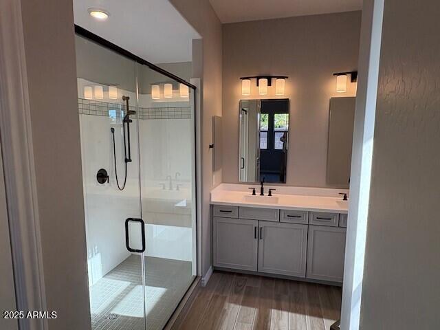 bathroom featuring double vanity, wood finished floors, a stall shower, and a sink