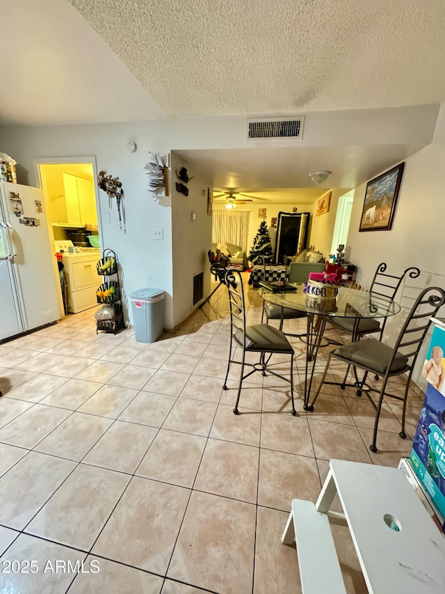 dining space featuring light tile patterned floors, a textured ceiling, washer and clothes dryer, and ceiling fan