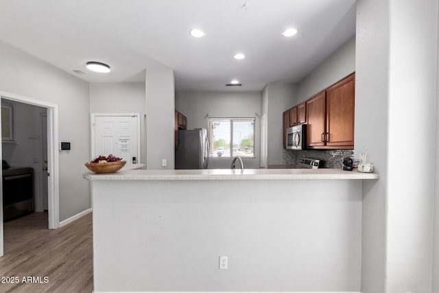 1102 N 5th St, Buckeye, AZ 85326 - kitchen featuring appliances with stainless steel finishes, brown cabinetry, a peninsula, light wood-style floors, and decorative backsplash
