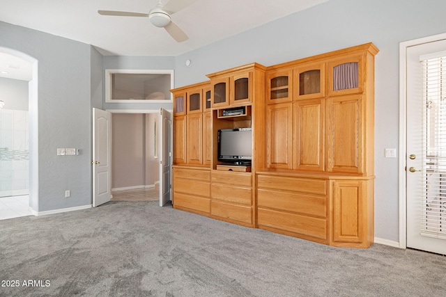 unfurnished bedroom featuring arched walkways, light colored carpet, baseboards, and ceiling fan