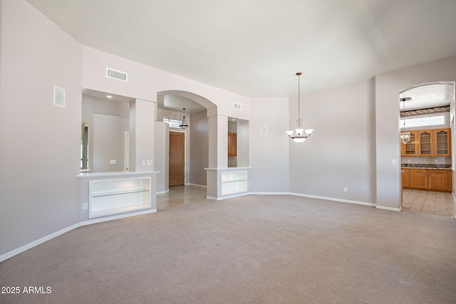unfurnished living room with a notable chandelier, baseboards, light carpet, visible vents, and arched walkways