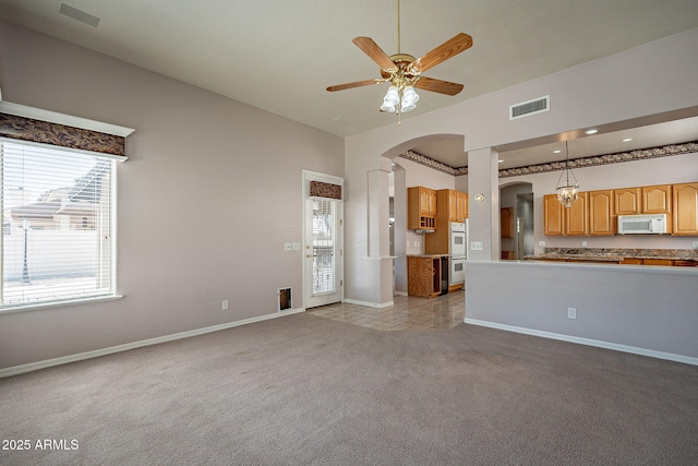 unfurnished living room featuring baseboards, a ceiling fan, visible vents, arched walkways, and light colored carpet