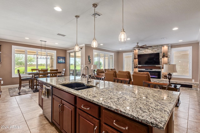 kitchen with pendant lighting, a stone fireplace, sink, ceiling fan, and an island with sink