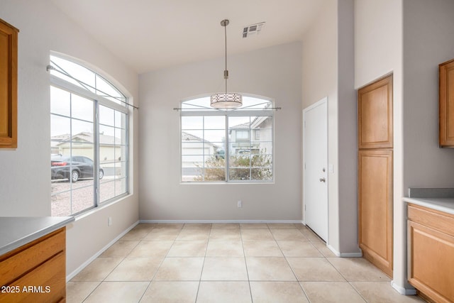 unfurnished dining area with lofted ceiling, light tile patterned flooring, baseboards, and visible vents