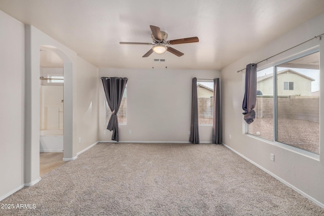 unfurnished room with visible vents, baseboards, carpet flooring, arched walkways, and a ceiling fan