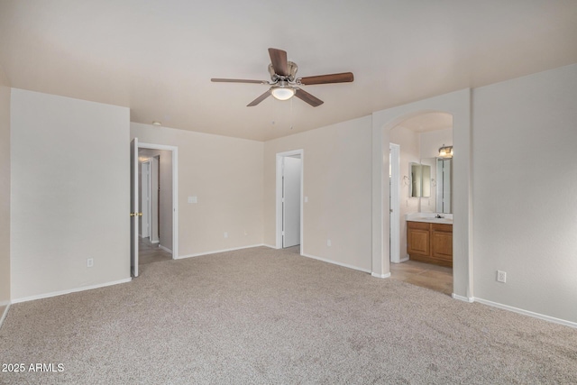 unfurnished bedroom with ensuite bathroom, a sink, arched walkways, baseboards, and light colored carpet