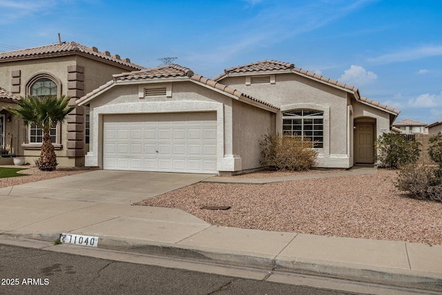 mediterranean / spanish house with a tile roof, an attached garage, driveway, and stucco siding