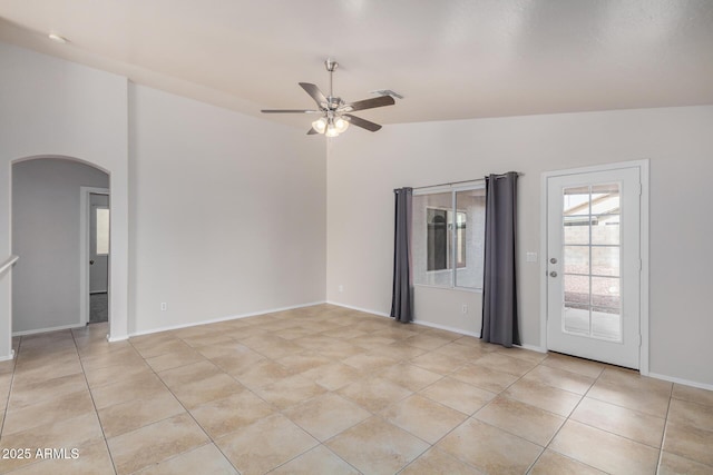 empty room with baseboards, ceiling fan, vaulted ceiling, light tile patterned flooring, and arched walkways