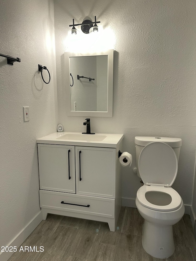bathroom featuring toilet, vanity, baseboards, and wood finished floors