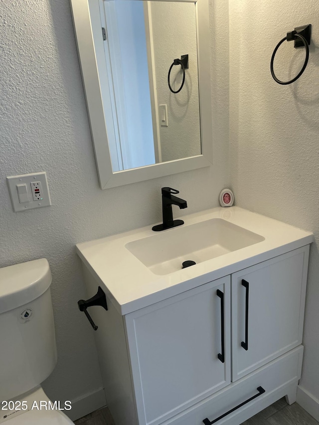 half bath featuring a textured wall, toilet, and vanity