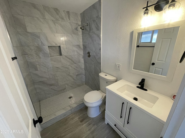 full bath featuring a tile shower, toilet, vanity, and wood finished floors