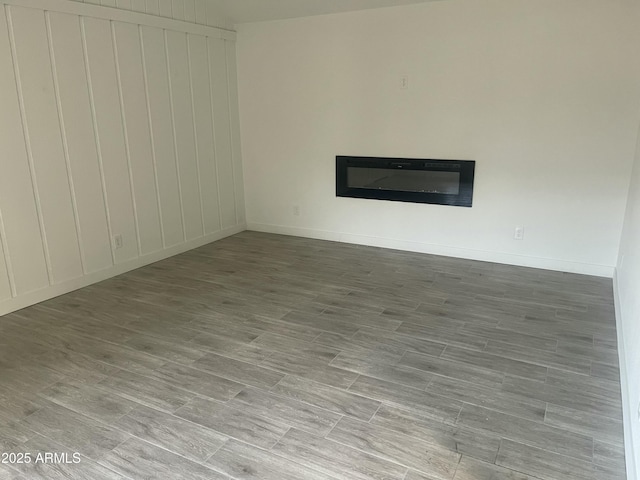 unfurnished room featuring baseboards, a glass covered fireplace, and wood finished floors