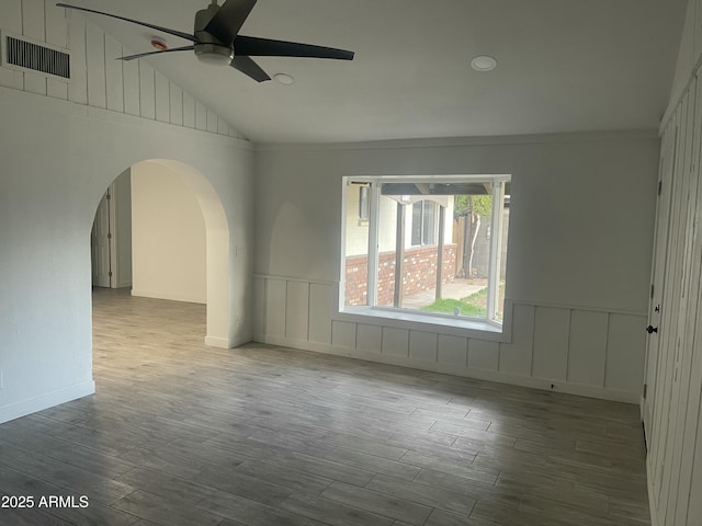 spare room featuring a ceiling fan, arched walkways, wood finished floors, and visible vents