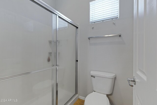 bathroom featuring a shower with door and toilet