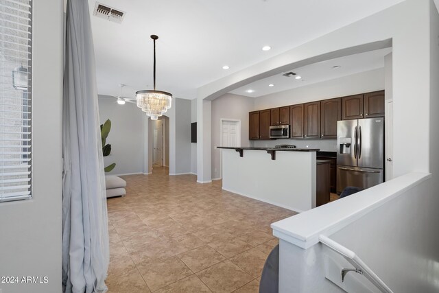 kitchen with dark brown cabinets, decorative light fixtures, a chandelier, stainless steel appliances, and a kitchen bar