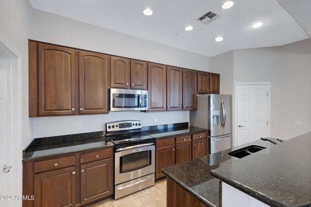 kitchen with dark stone countertops, appliances with stainless steel finishes, light tile patterned floors, and sink