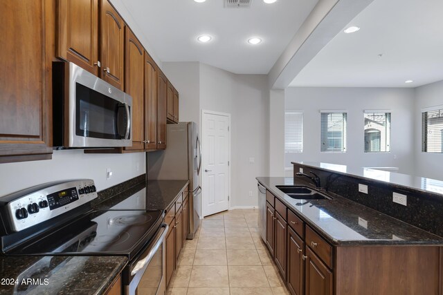 kitchen with dark stone counters, sink, light tile patterned floors, and stainless steel appliances