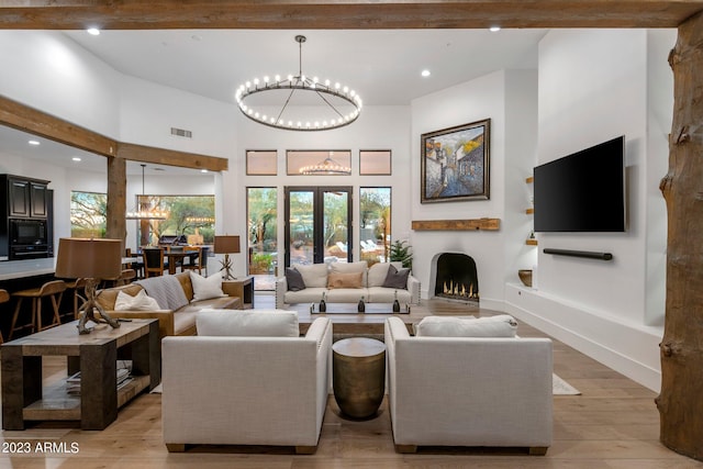 living room featuring beam ceiling, a towering ceiling, a notable chandelier, and light wood-type flooring